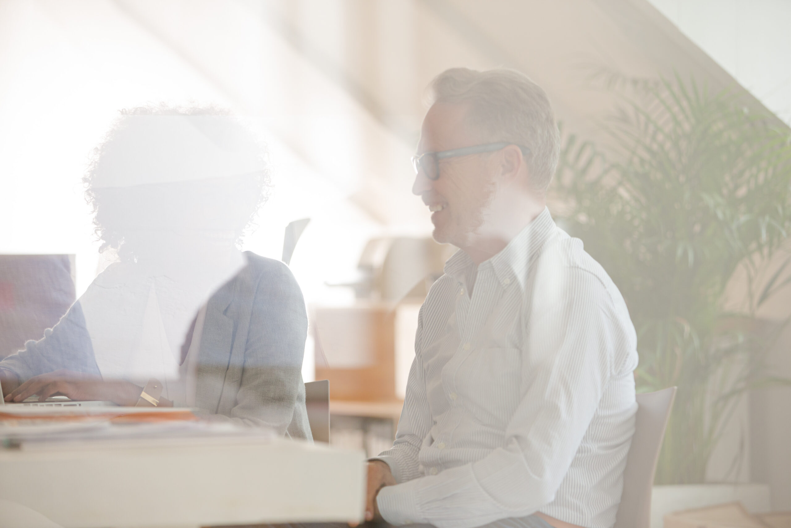 Two office workers talking at desk using laptop